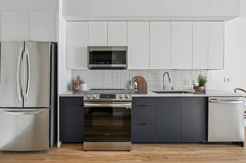 Studio Apartments in Santa Monica, CA - Kitchen with Stainless Steel Efficient Appliances, Wood-Like Flooring, Dual Colored Modern Cabinets, and White Tile Backsplash